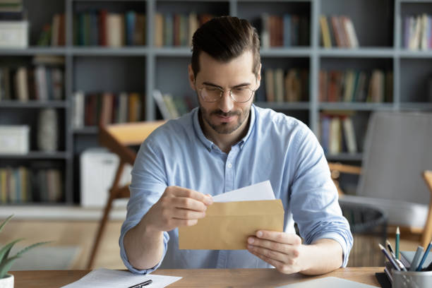 Serious businessman sit at desk holding envelope take out letter Serious businessman sit at workplace office desk holding envelope take out letter feels interested read business news, got invitation, learns bank statement information. Postal correspondence concept letter of intent stock pictures, royalty-free photos & images