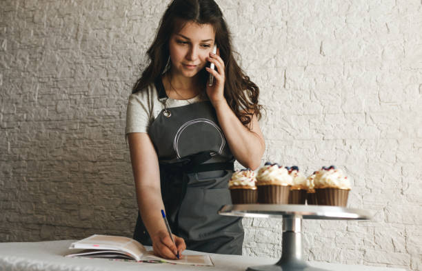 the cook girl is talking on the phone taking an order from a customer. the cook girl is talking on the phone taking an order from a customer Home Baking Business stock pictures, royalty-free photos & images