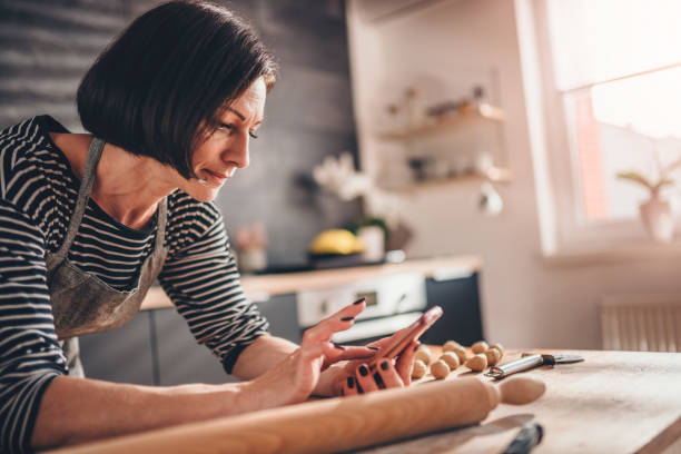 Woman searching apple pie recipe on the smart phone Woman standing in the kitchen by the wooden table and searching apple pie recipe on the smart phone Home Baking Business stock pictures, royalty-free photos & images