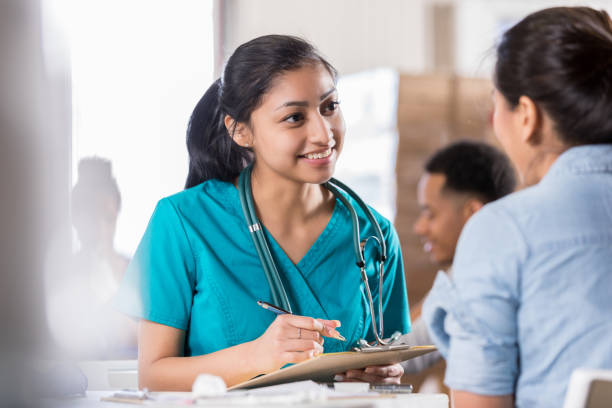 Attentive young doctor talks with female patient Young female Hispanic volunteer healthcare professional talks with female patient about her medical history. organizations that help patients stock pictures, royalty-free photos & images