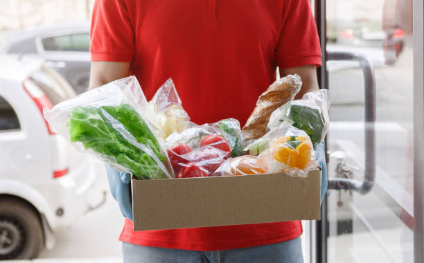 Delivery of products from supermarket during epidemic. Courier holding box of groceries. Delivery of products from supermarket during epidemic. Courier in medical gloves holding box of groceries, at the entrance Delivering Grocies stock pictures, royalty-free photos & images