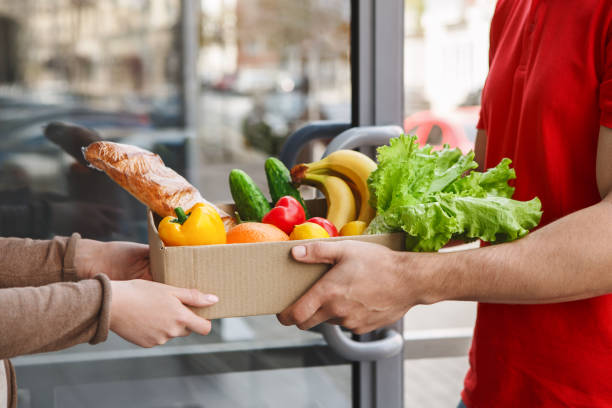 Purchasing food by courier. Deliveryman gives box of products to girl Purchasing food by courier. Deliveryman gives box of products to girl home, side view, close up Delivering Grocies stock pictures, royalty-free photos & images