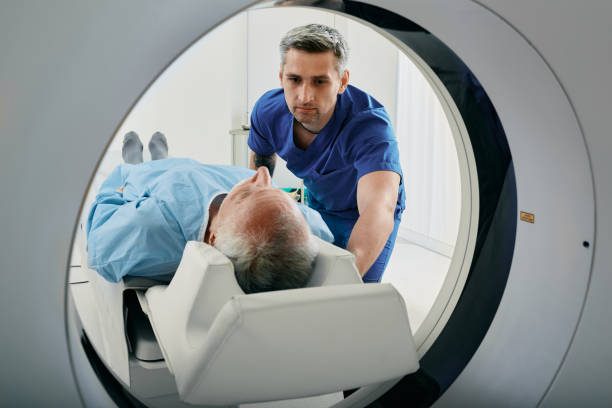 Senior man going into CT scanner. CT scan technologist overlooking patient in Computed Tomography scanner during preparation for procedure Senior man going into CT scanner. CT scan technologist overlooking patient in Computed Tomography scanner during preparation for procedure cancer patients stock pictures, royalty-free photos & images