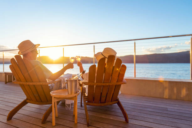 Couple relaxing and drinking wine and toasting on deck chairs Couple relaxing and drinking wine and toasting on deck chairs in an over water bungalow. They are looking at the view Travelling to Australia stock pictures, royalty-free photos & images