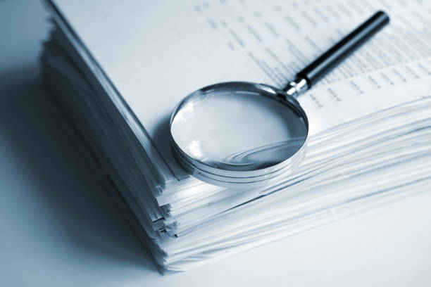Magnifying glass on a stack of documents Magnifying glass on a stack of documents Bank Documentation stock pictures, royalty-free photos & images