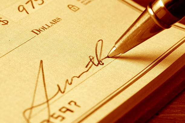 Signing a Check "Hand signing a check, gold toned.  ***Please note: the number visible is the check number and not an account number.  The signature is fictitious.  No personal information is visible." Writing cheque stock pictures, royalty-free photos & images